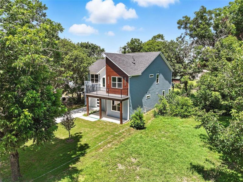 Back of house with a patio area, a yard, roof with shingles, and view of wooded area