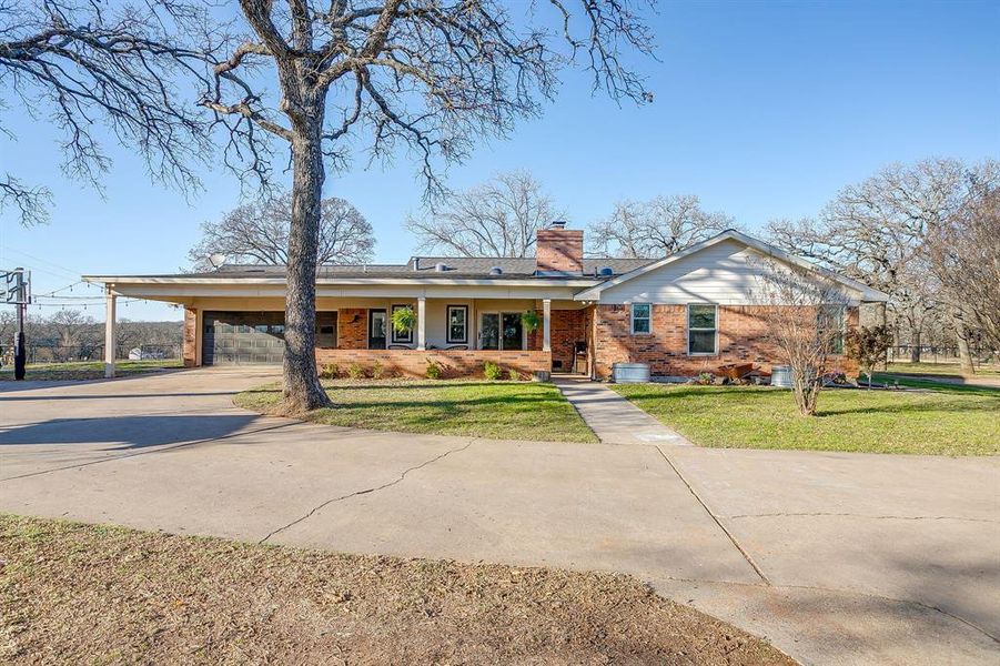 Ranch-style home featuring covered porch, a chimney, brick siding, driveway, and a front lawn
