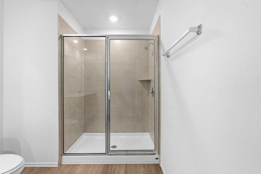 Glass-enclosed shower with tile surround, built-in shelving, white shower pan, and chrome fixtures
