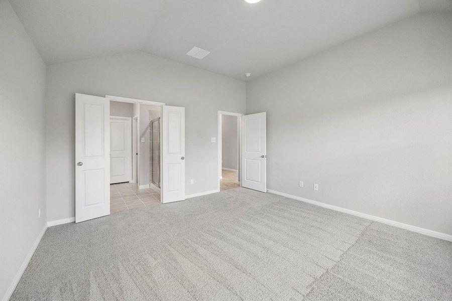 An airy bedroom with vaulted ceilings offers soft carpeting and seamless access to an ensuite bathroom.