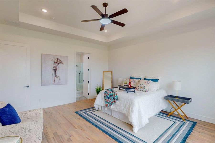 Bedroom with a raised ceiling, connected bathroom, light hardwood / wood-style flooring, and ceiling fan