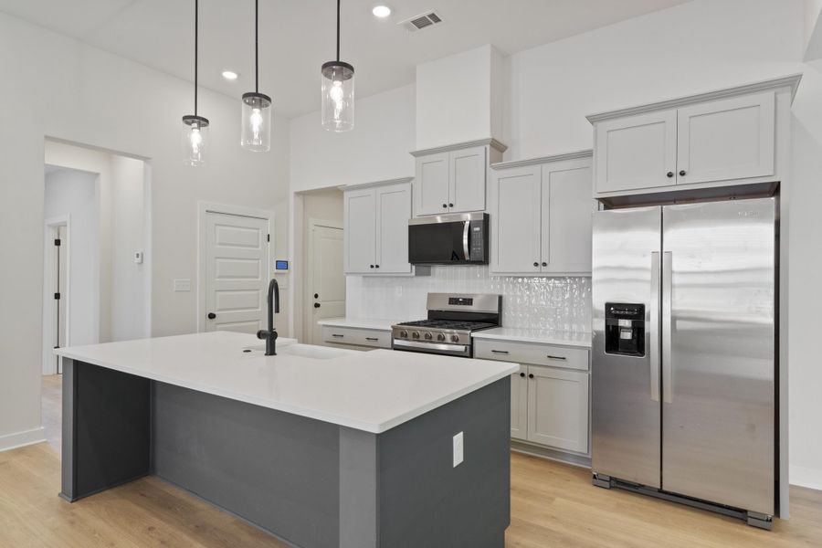 Kitchen featuring a central island with white countertop, light wood-finish flooring, white subway tile backsplash, stainless steel appliances, and ceiling-mounted pendant lighting