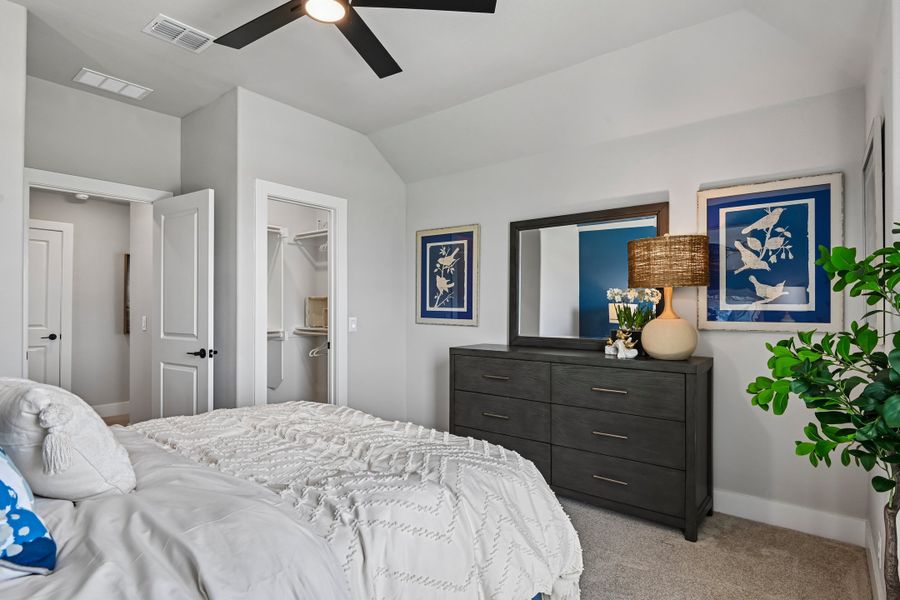 Bedroom with vaulted ceiling, ceiling fan, dark wood dresser, and walk-in closet visible in background