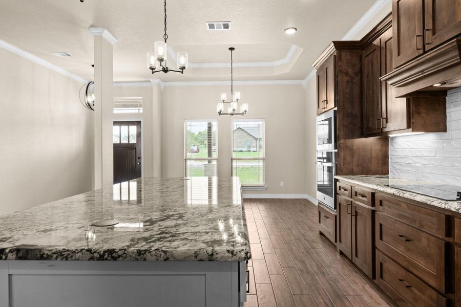Kitchen with light granite counters, decorative light fixtures, a tray ceiling, crown molding, and backsplash Kitchen with light granite counters, decorative light fixtures, a tray ceiling, crown molding, and backsplash