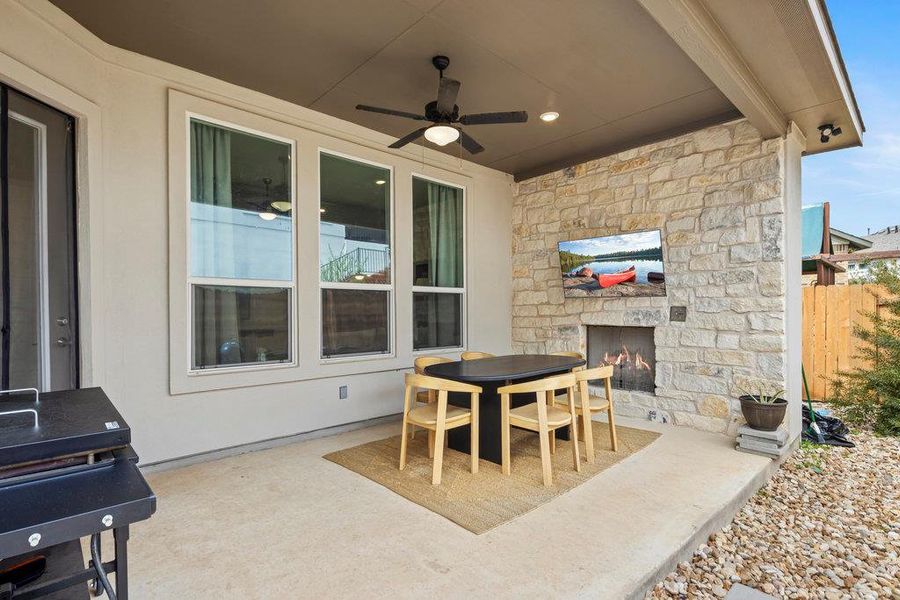 View of patio featuring outdoor dining space, a ceiling fan, fence, and an outdoor stone fireplace