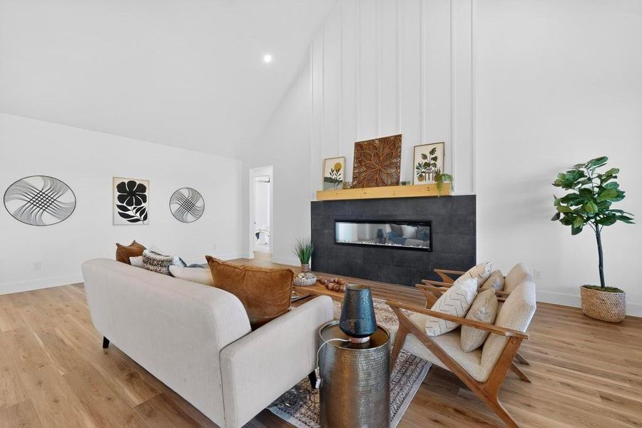 Living room featuring a glass covered fireplace, light wood finished floors, and lofted ceiling Living room featuring a glass covered fireplace, light wood finished floors, and lofted ceiling
