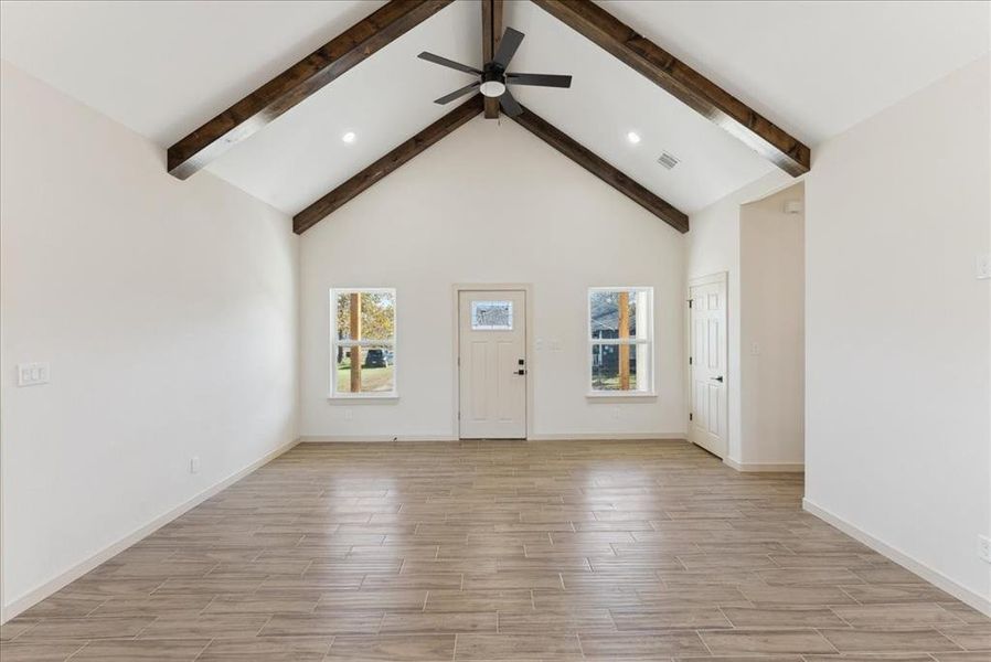 Unfurnished living room featuring ceiling fan, beamed ceiling, high vaulted ceiling, and light wood-type flooring