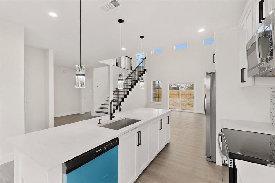 Kitchen with a kitchen island with sink, white cabinets, stainless steel appliances, pendant lighting, and a high ceiling Kitchen with a kitchen island with sink, white cabinets, stainless steel appliances, pendant lighting, and a high ceiling