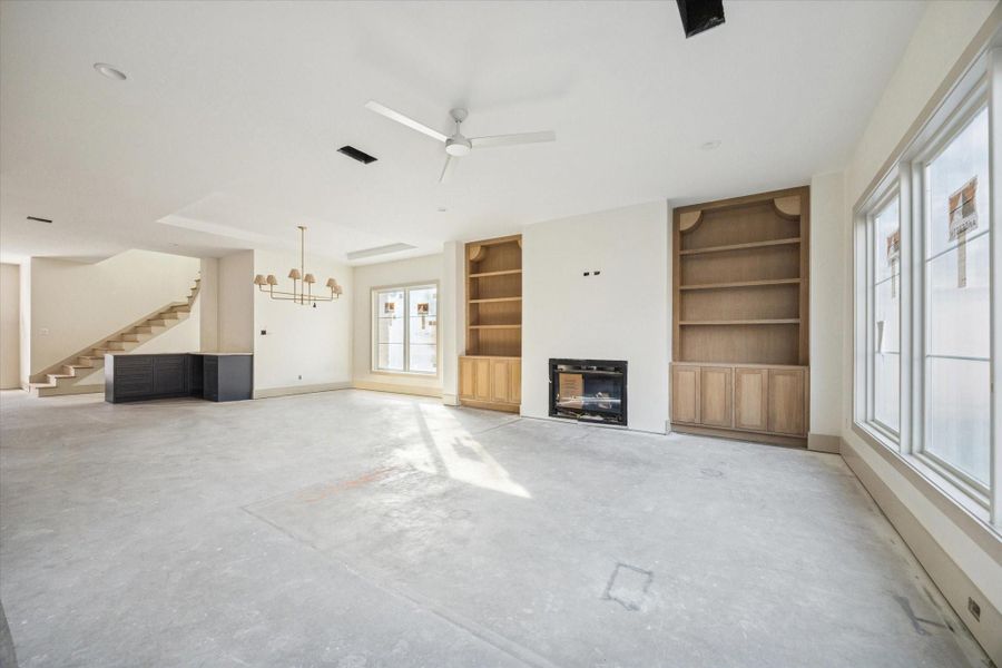 LIVING ROOM - Expansive living area features custom built in shelving, a fireplace flanked by warm wood cabinetry, and oversized windows that flood the space with natural light. Clean ceiling lines and thoughtful proportions create an open setting designed for both everyday living and effortless entertaining. -- Construction as of 1/5/26