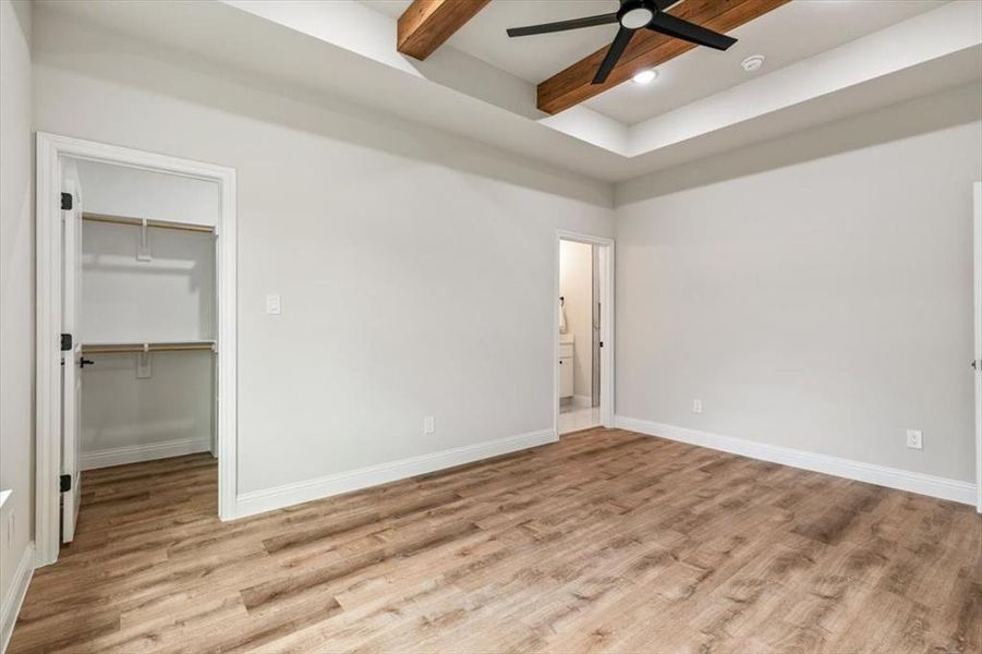 Spacious room featuring wood-finish flooring, a tray ceiling with exposed wood beams, and a ceiling fan