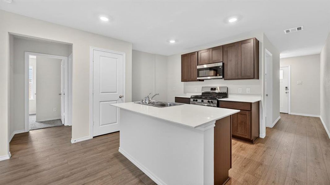 Kitchen featuring a central island with an undermount sink, dark wood cabinetry, stainless steel appliances, white countertops, and wood-finish flooring