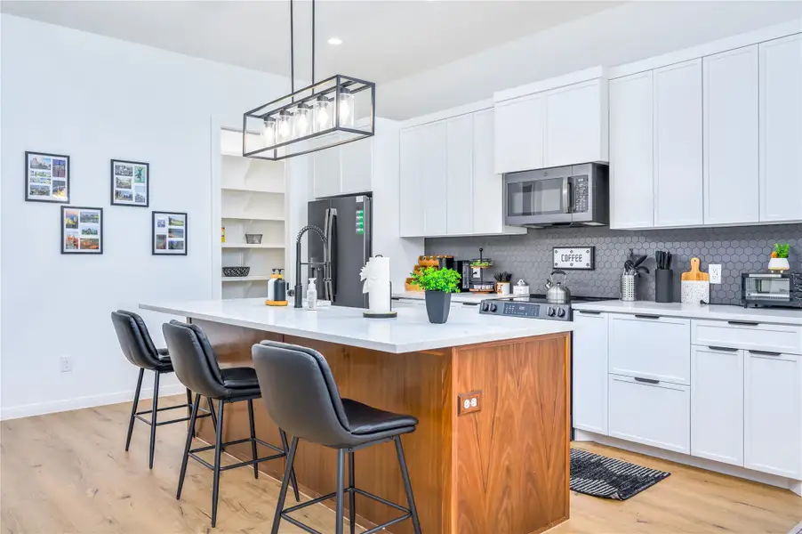 Kitchen featuring white and natural cabinetry, an island with sink, pendant lighting, and light wood-type flooring.