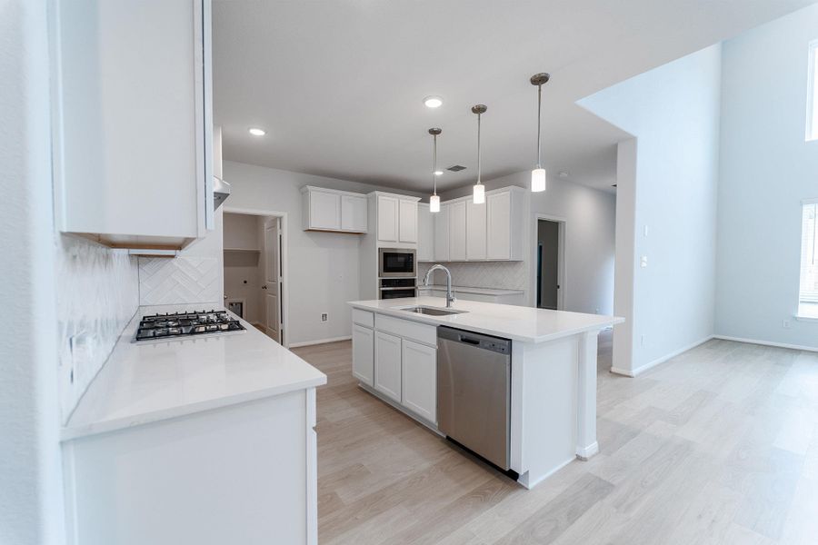 Kitchen with white cabinets, stainless steel appliances, an island with sink, and light stone countertops