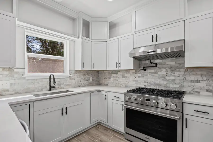 Kitchen featuring high end stainless steel range, under cabinet range hood, white cabinets, wood finish floors, and light stone counters Kitchen featuring high end stainless steel range, under cabinet range hood, white cabinets, wood finish floors, and light stone counters