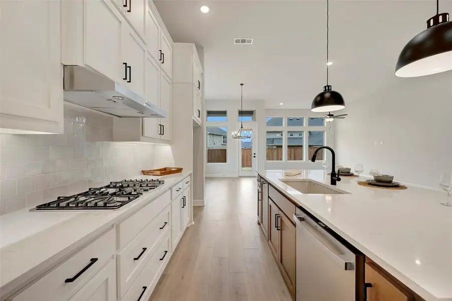 Dual tone kitchen with dual tone cabinetry, stainless steel appliances, light wood-style flooring, pendant lighting, and light stone counters