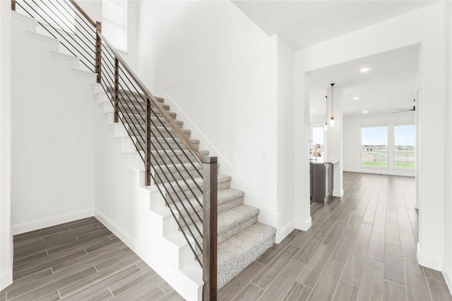 Entryway with carpeted staircase, metal railing, wood-look tile floors, and open view to kitchen and living area Entryway with carpeted staircase, metal railing, wood-look tile floors, and open view to kitchen and living area