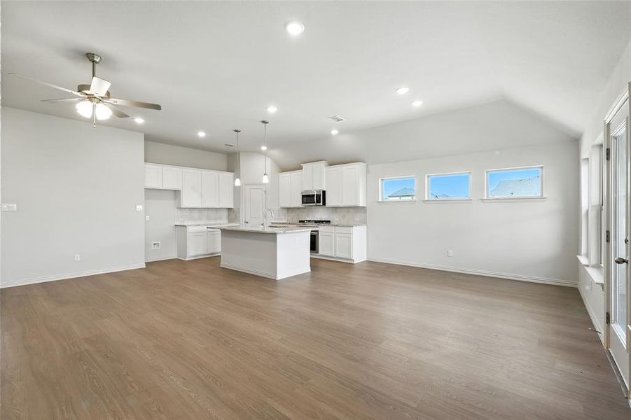 Kitchen with lofted ceiling, white cabinets, open floor plan, an island with sink, and decorative backsplash Kitchen with lofted ceiling, white cabinets, open floor plan, an island with sink, and decorative backsplash
