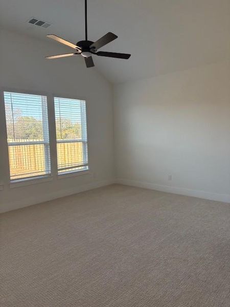 Empty room featuring ceiling fan, lofted ceiling, light carpet, visible vents, and baseboards