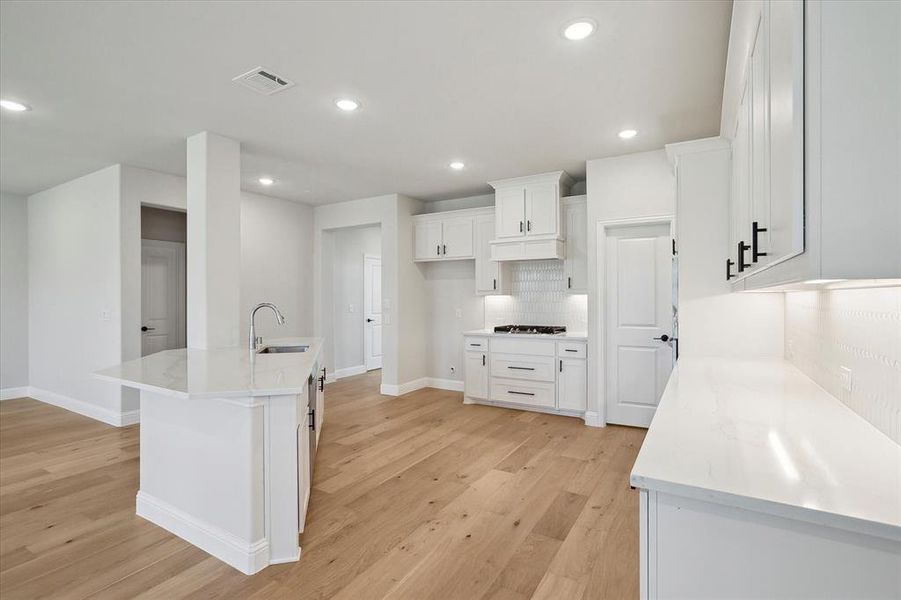 Kitchen with a sink, gas cooktop, light wood-style floors, white cabinetry, and recessed lighting