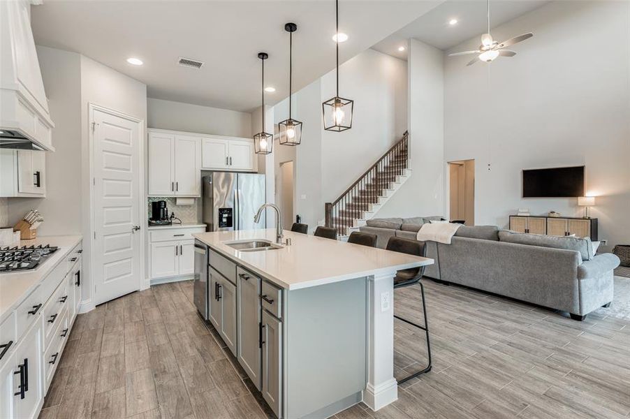 Kitchen featuring appliances with stainless steel finishes, white cabinets, sink, custom exhaust hood, and an island with sink