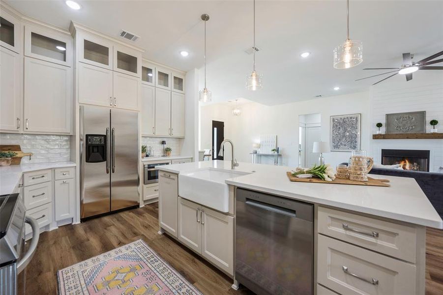 Gourmet kitchen featuring expansive island with farmhouse sink and breakfast bar seating. Abundant storage throughout with stunning greige floor-to-ceiling cabinetry and decorative glass uppers. Complete with electric range and hood, dishwasher, and convenient microwave drawer.