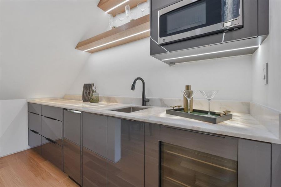 Contemporary wet bar featuring a stainless steel sink, dark cabinetry, and light stone countertops
