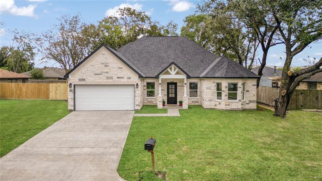 This is a single-story home featuring a two-car garage, stone and siding exterior, and a well-maintained lawn. Mature trees add character to the property, which is enclosed by a wooden privacy fence.