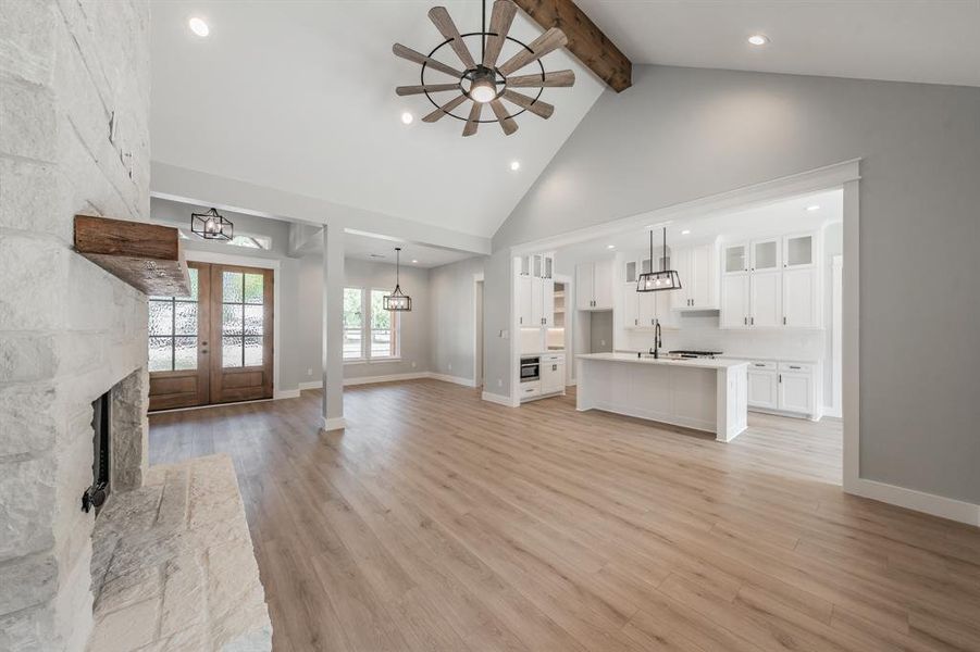 Unfurnished living room with high vaulted ceiling, a stone fireplace, beam ceiling, ceiling fan, and light hardwood / wood-style flooring