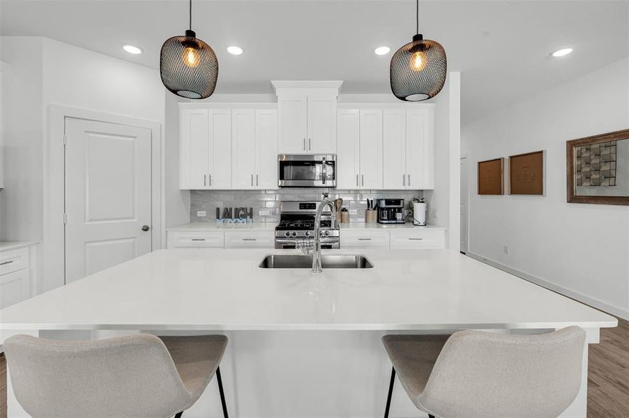 Kitchen featuring sink, white cabinetry, decorative light fixtures, a center island with sink, and stainless steel appliances