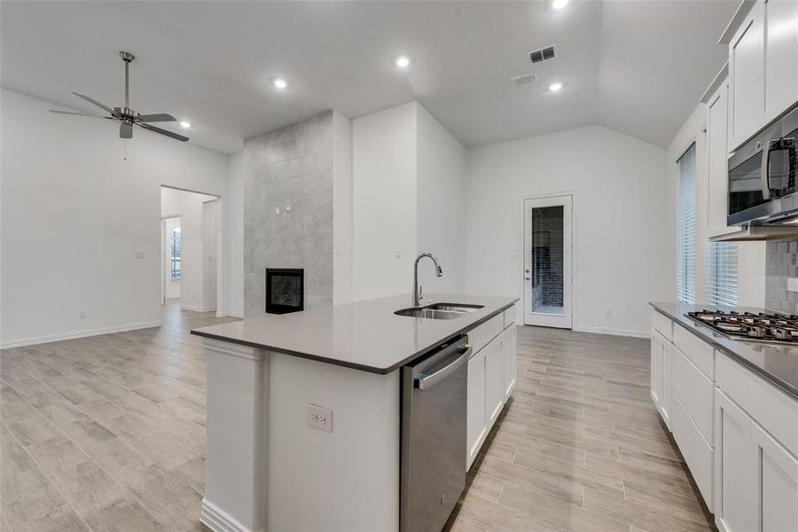 Kitchen featuring lofted ceiling, stainless steel appliances, a tile fireplace, sink, and ceiling fan