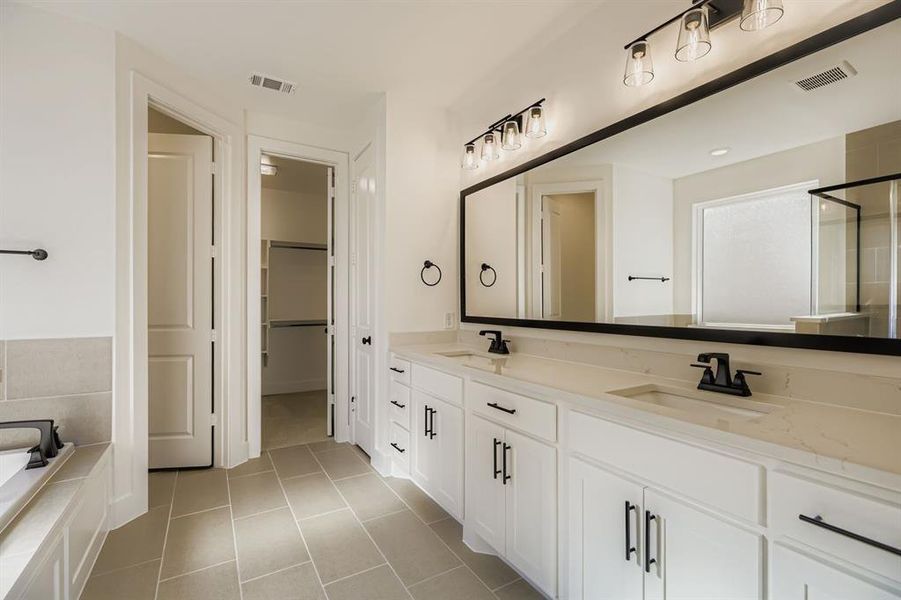 Bathroom with double vanity, light tile patterned floors, a relaxing tiled tub, and a walk in closet