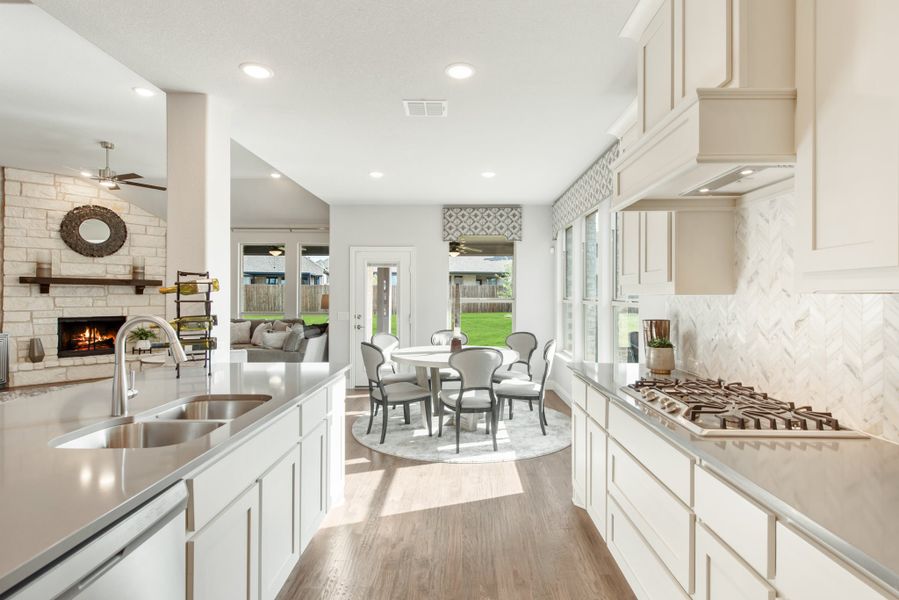 Open kitchen with white cabinets, gas cooktop, and view into dining area and living room with stone fireplace