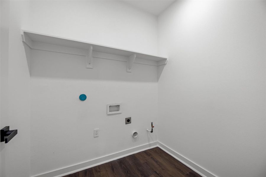 Laundry room with hookups for a washer and dryer. It features white walls, a high shelf for storage, and dark wood flooring. Laundry room with hookups for a washer and dryer. It features white walls, a high shelf for storage, and dark wood flooring.
