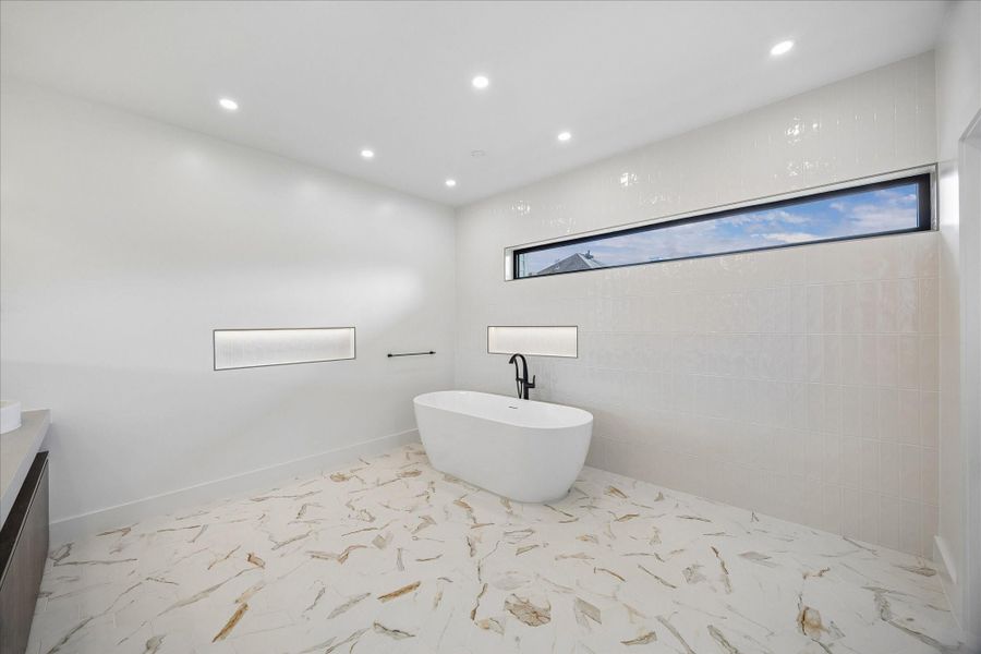 Luxurious bathroom featuring a freestanding tub, elegant tile flooring, and modern recessed lighting, complemented by a stylish horizontal window for natural light. Luxurious bathroom featuring a freestanding tub, elegant tile flooring, and modern recessed lighting, complemented by a stylish horizontal window for natural light.