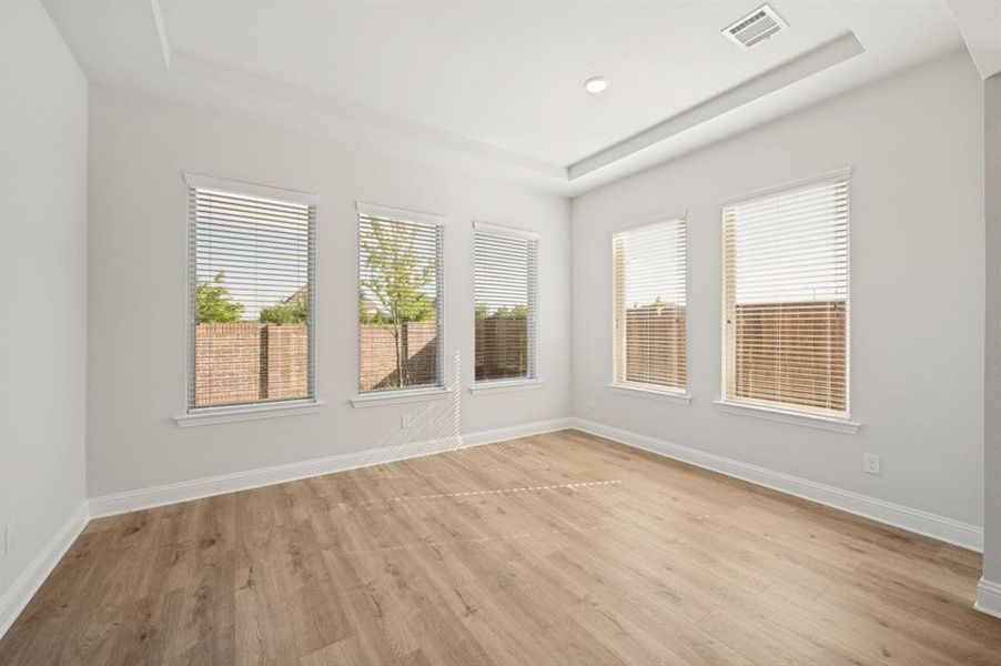 Spacious room featuring four large windows with blinds, wood-finish flooring, white baseboards, and a tray ceiling with recessed lighting