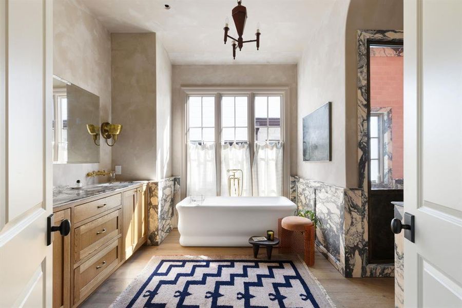 Full bath featuring light wood-type flooring, a soaking tub, vanity, tile walls, and wainscoting