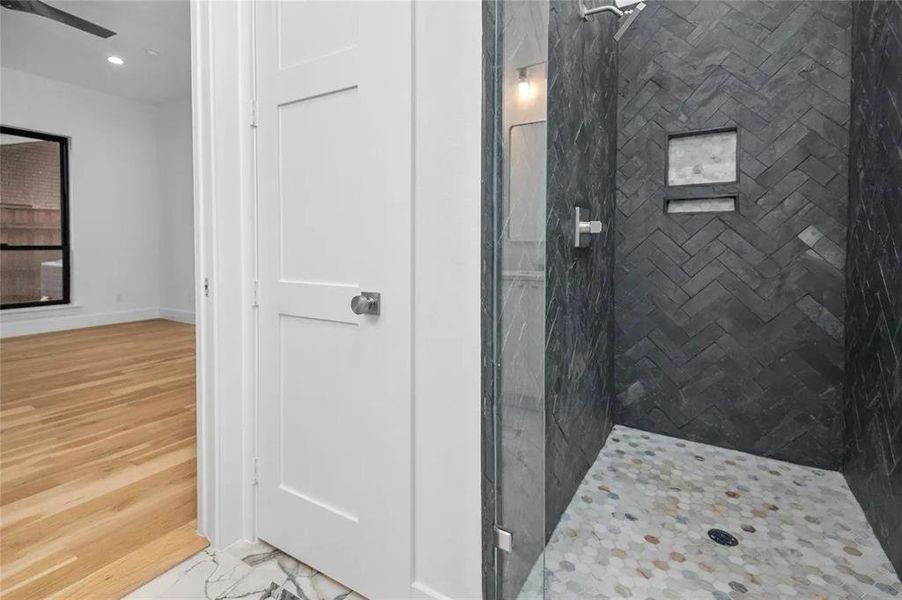 Walk-in shower featuring dark herringbone tile walls, an integrated niche, and a hexagonal tile floor Walk-in shower featuring dark herringbone tile walls, an integrated niche, and a hexagonal tile floor