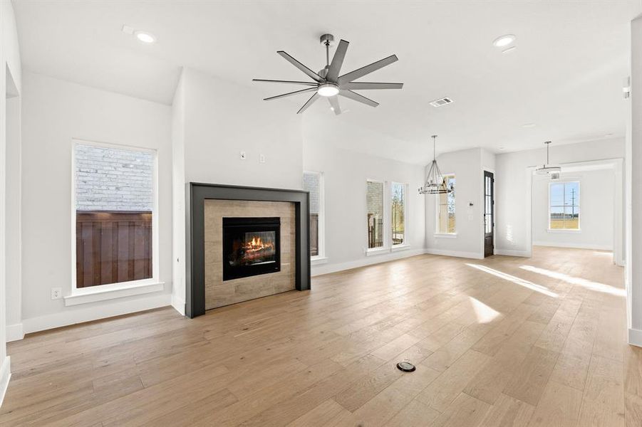 Unfurnished living room with a tiled fireplace, a healthy amount of sunlight, ceiling fan with notable chandelier, and light hardwood / wood-style floors