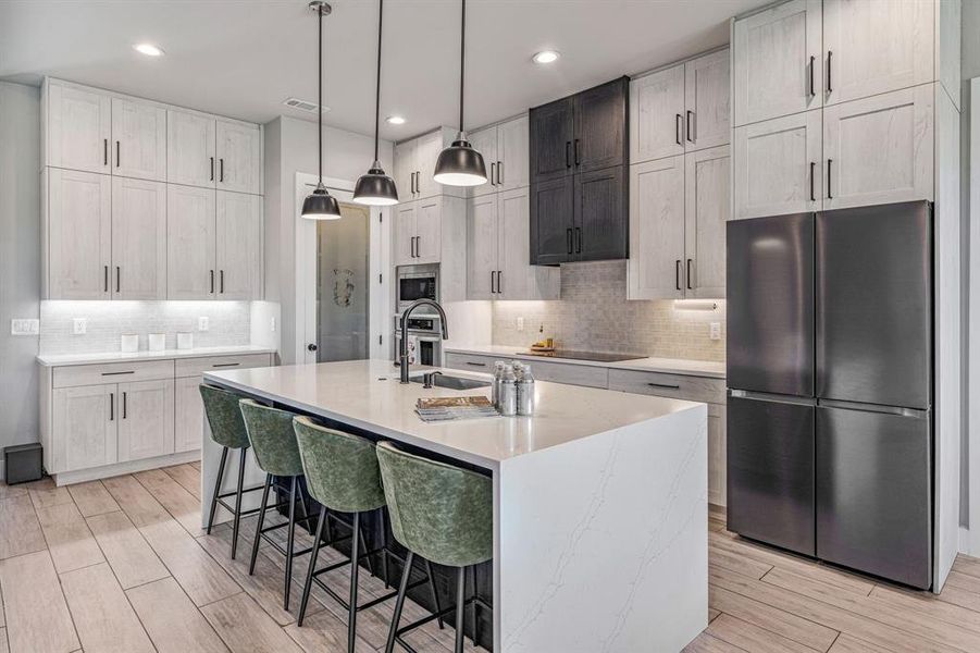 Kitchen with stainless steel appliances, a breakfast bar area, a center island with sink, wood tiled floors, and hanging light fixtures