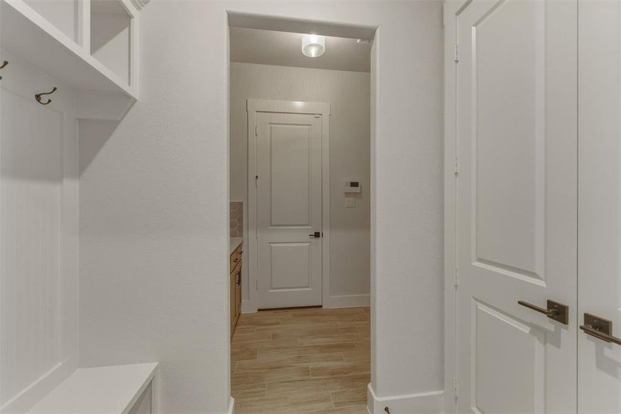 Entryway featuring built-in storage with coat hooks, white paneled doors with bronze hardware, and wood-finish tile flooring Entryway featuring built-in storage with coat hooks, white paneled doors with bronze hardware, and wood-finish tile flooring