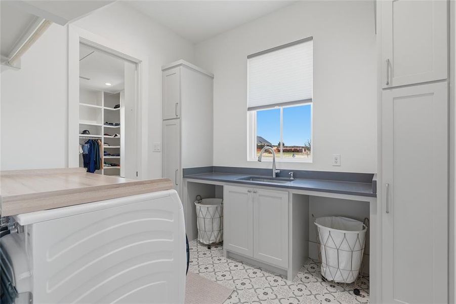 Bright utility room featuring custom cabinetry, a built-in sink with a gooseneck faucet, patterned floor tiling, and a window with a pleated shade