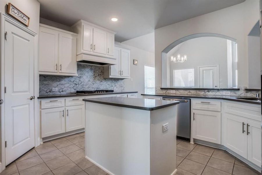 Kitchen with white cabinets, backsplash, appliances with stainless steel finishes, premium range hood, and light tile patterned floors