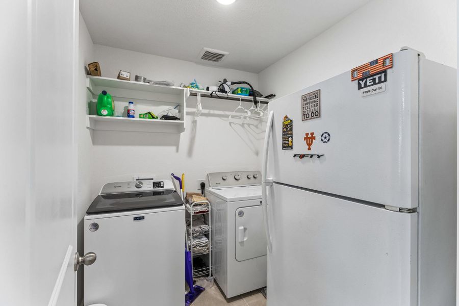 Dedicated laundry area featuring a top-load washing machine, a front-load dryer, and overhead shelving for storage