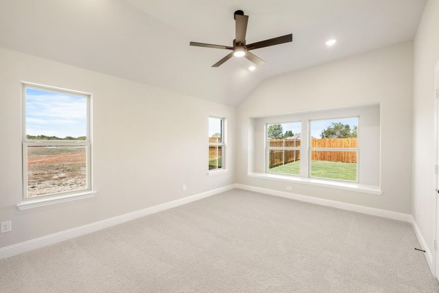 Empty bedroom with vaulted ceiling, ceiling fan, carpet flooring, and multiple windows overlooking backyard Empty bedroom with vaulted ceiling, ceiling fan, carpet flooring, and multiple windows overlooking backyard
