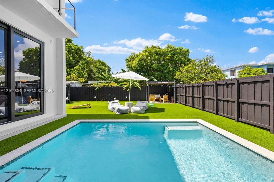 Private backyard featuring a rectangular swimming pool with a sun shelf, synthetic turf lawn, and full-perimeter horizontal wood-style fencing