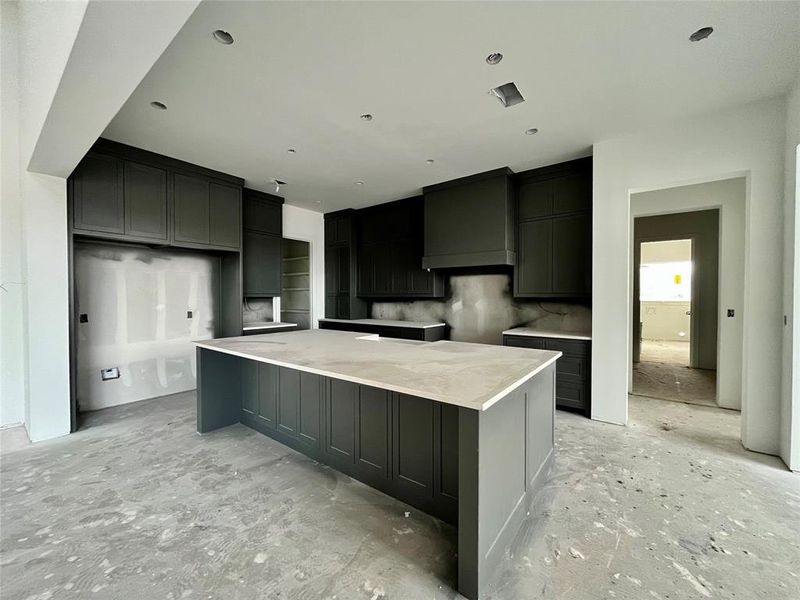 Kitchen with tasteful backsplash, light stone countertops, a spacious island, and custom range hood