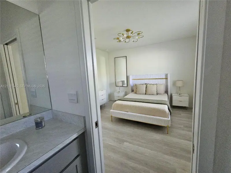 Bathroom featuring a stone-top vanity with an integrated sink and a large wall-mounted mirror, wood-finish flooring throughout, and a multi-light flush mount ceiling fixture