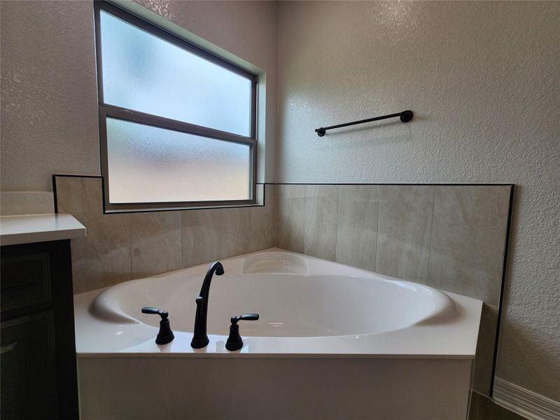 Corner tub with elegant dark fixtures and a frosted window for privacy. Corner tub with elegant dark fixtures and a frosted window for privacy.