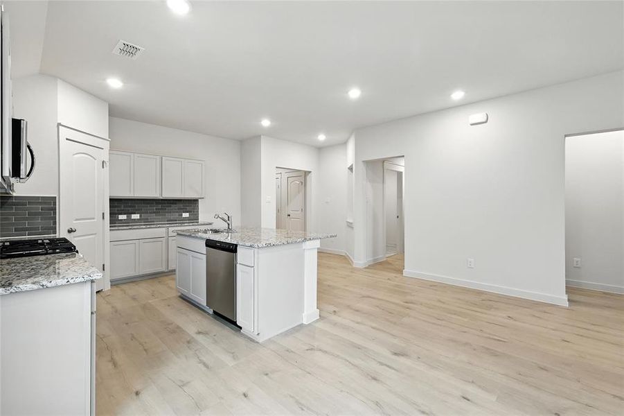 Kitchen featuring stainless steel appliances, backsplash, light wood-type flooring, a kitchen island with sink, and recessed lighting