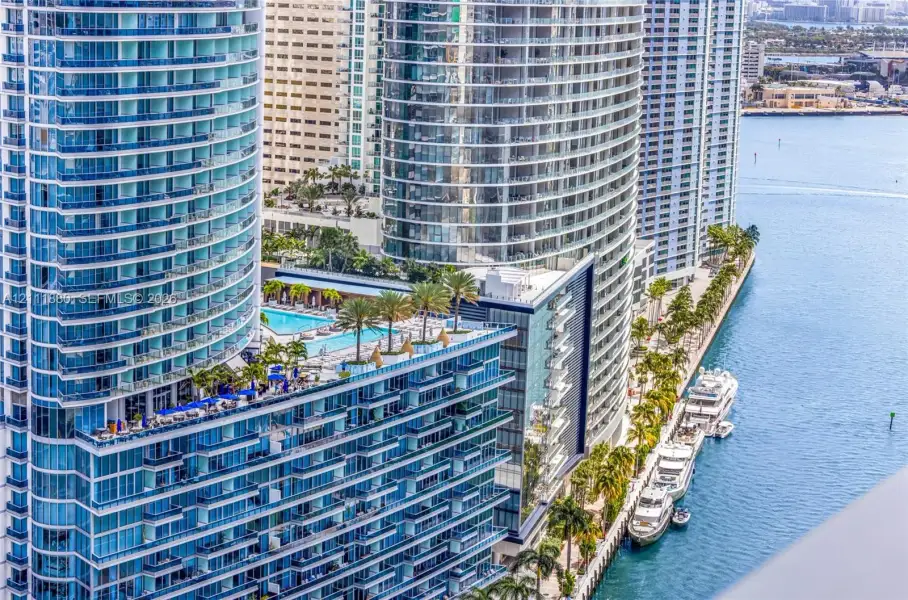 High-rise residential exterior featuring floor-to-ceiling glass paneling, wrap-around balconies, an elevated swimming pool deck, and deep-water marina access